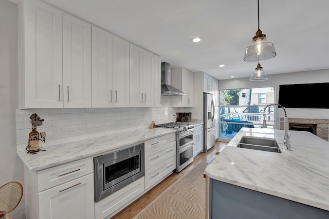 kitchen featuring stainless steel appliances, wall chimney range hood, white cabinetry, and sink