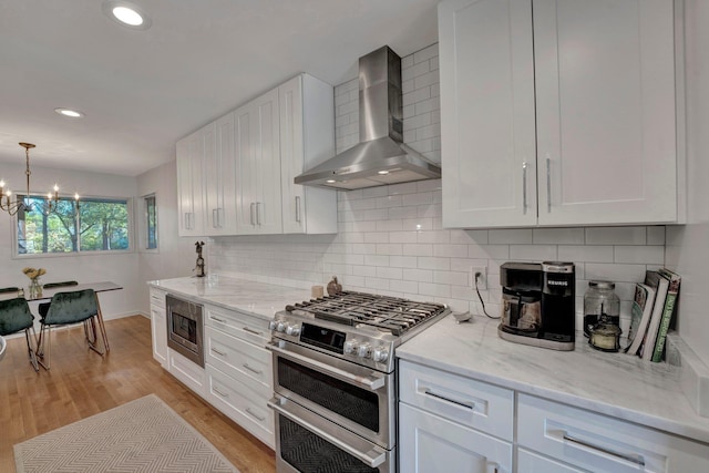 kitchen with stainless steel appliances, white cabinetry, backsplash, wall chimney range hood, and pendant lighting