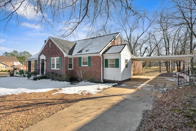 view of snow covered exterior with a carport, concrete driveway, and brick siding