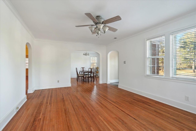 empty room featuring ceiling fan with notable chandelier, wood-type flooring, plenty of natural light, and crown molding