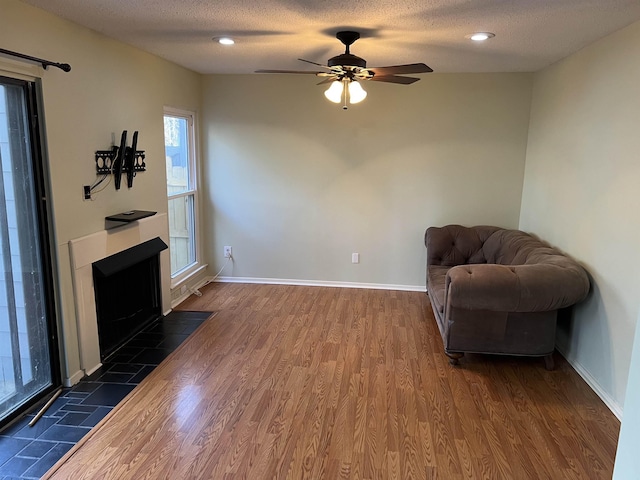 living area featuring ceiling fan, dark wood-type flooring, a tile fireplace, and a textured ceiling