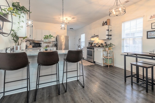 kitchen with a chandelier, appliances with stainless steel finishes, dark wood-type flooring, a wealth of natural light, and white cabinets