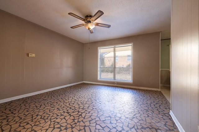 unfurnished room featuring a textured ceiling, ceiling fan, and wood walls