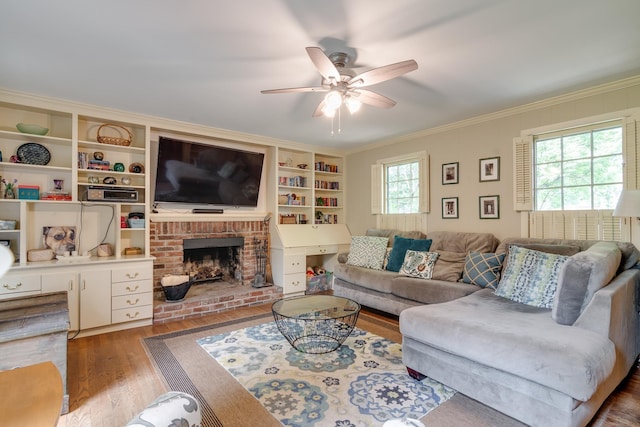 living room with wood-type flooring, ornamental molding, ceiling fan, a fireplace, and built in shelves