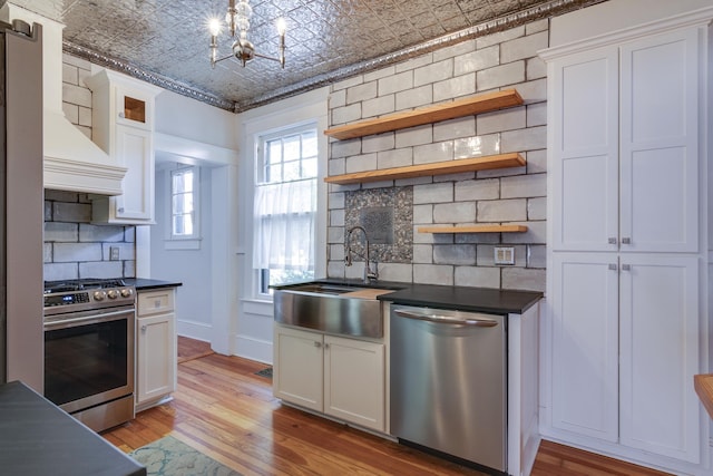 kitchen with white cabinets, light wood-type flooring, appliances with stainless steel finishes, and backsplash