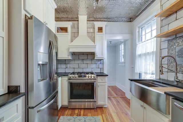 kitchen featuring white cabinets, custom exhaust hood, appliances with stainless steel finishes, and backsplash