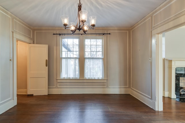 unfurnished dining area with a fireplace, an inviting chandelier, dark wood-type flooring, and ornamental molding