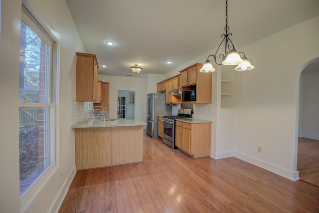 kitchen with a chandelier, appliances with stainless steel finishes, hanging light fixtures, light wood-type flooring, and backsplash