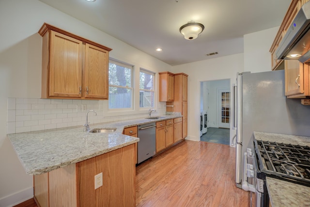 kitchen featuring kitchen peninsula, light stone countertops, extractor fan, stainless steel appliances, and sink