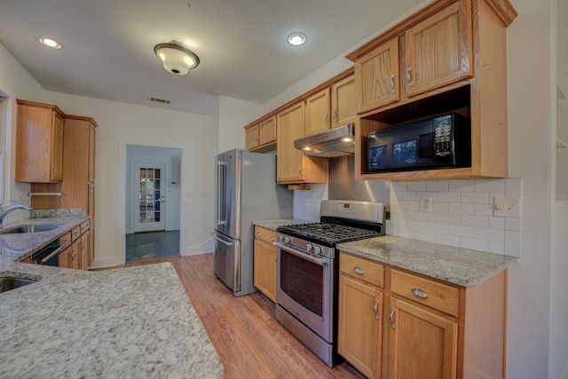 kitchen with stainless steel appliances, light stone counters, decorative backsplash, sink, and light hardwood / wood-style flooring