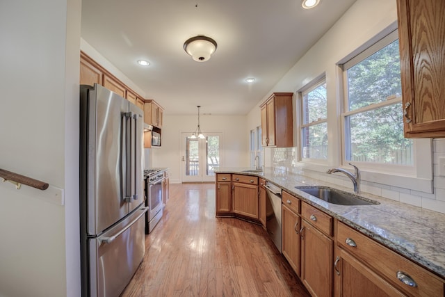 kitchen with sink, tasteful backsplash, light hardwood / wood-style flooring, hanging light fixtures, and high quality appliances