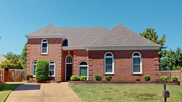 view of front of property with brick siding, fence, a front lawn, and roof with shingles