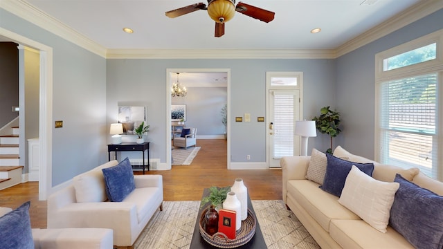 living room featuring crown molding, light wood finished floors, stairway, baseboards, and ceiling fan with notable chandelier