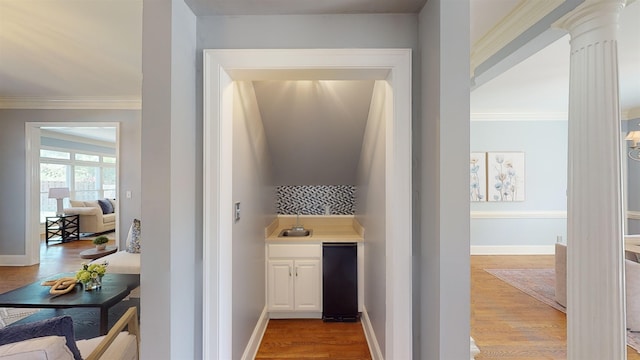 bar featuring ornamental molding, baseboards, a sink, and light wood finished floors