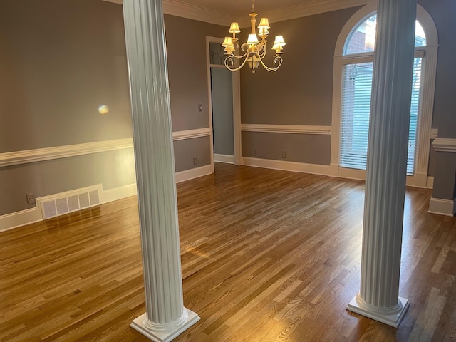 unfurnished dining area featuring visible vents, wood finished floors, crown molding, ornate columns, and a chandelier