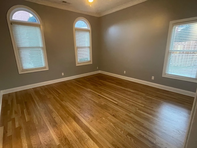 unfurnished room with crown molding, a healthy amount of sunlight, dark wood finished floors, and baseboards