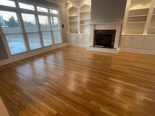 unfurnished living room featuring baseboards, light wood finished floors, a premium fireplace, and built in features