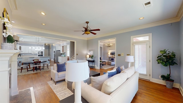 living room featuring crown molding, recessed lighting, wood finished floors, baseboards, and ceiling fan with notable chandelier