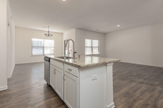 kitchen with light stone countertops, white cabinetry, an island with sink, sink, and hanging light fixtures