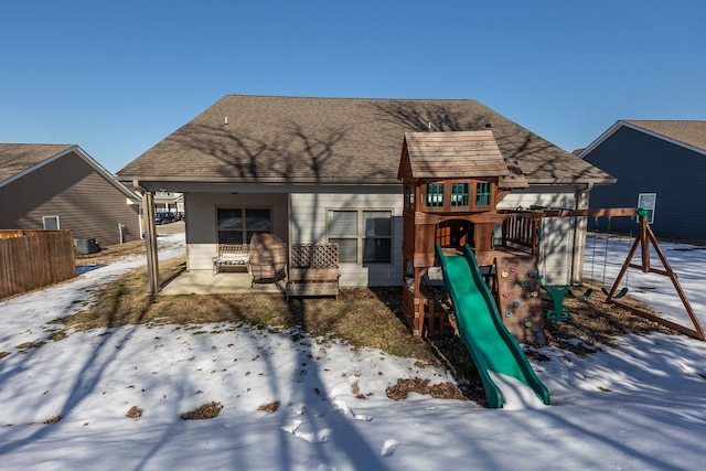 snow covered back of property with a playground and cooling unit