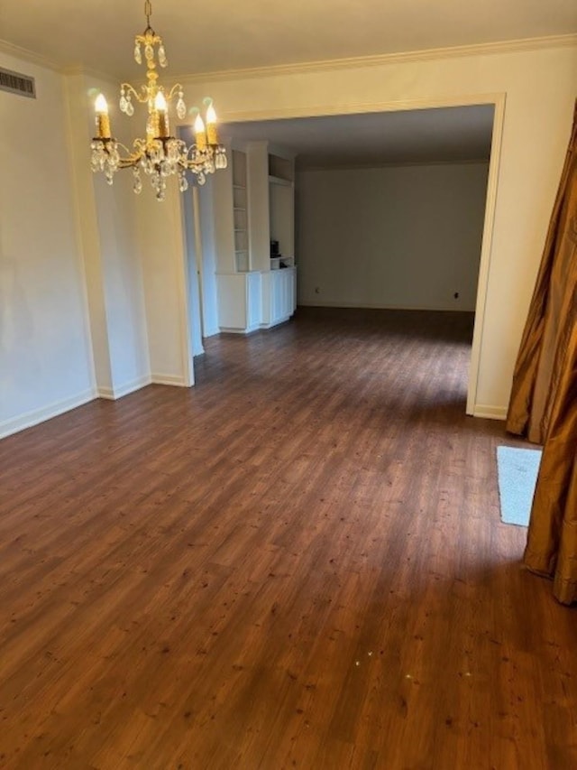 spare room featuring dark wood-type flooring, ornamental molding, and a chandelier