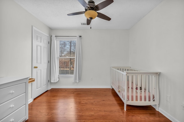 unfurnished bedroom with ceiling fan, hardwood / wood-style flooring, a textured ceiling, and a nursery area