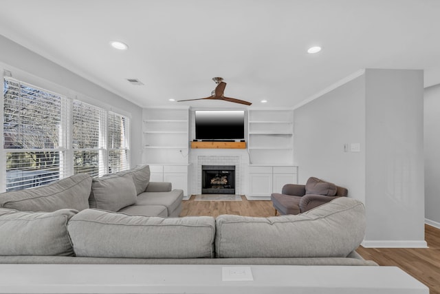 living room featuring ceiling fan, built in features, a fireplace, and light hardwood / wood-style flooring