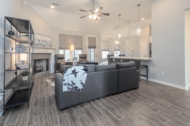 living room featuring ceiling fan, sink, a tile fireplace, and vaulted ceiling