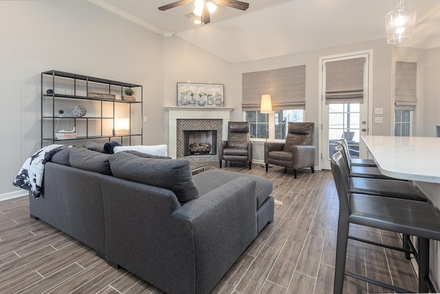 living room featuring ceiling fan, a tile fireplace, ornamental molding, and lofted ceiling