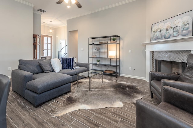 living room featuring ceiling fan, crown molding, and a tiled fireplace