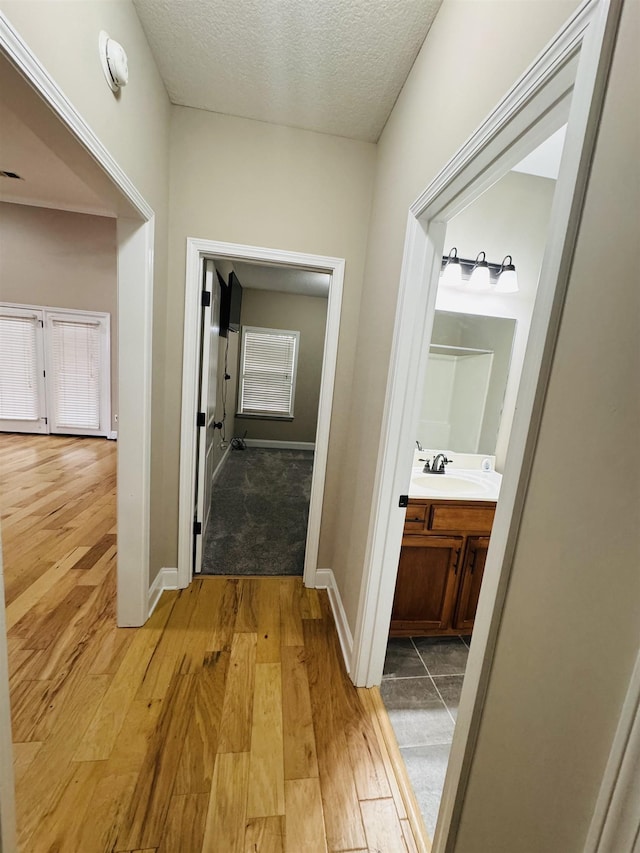 hall featuring light hardwood / wood-style floors, sink, and a textured ceiling