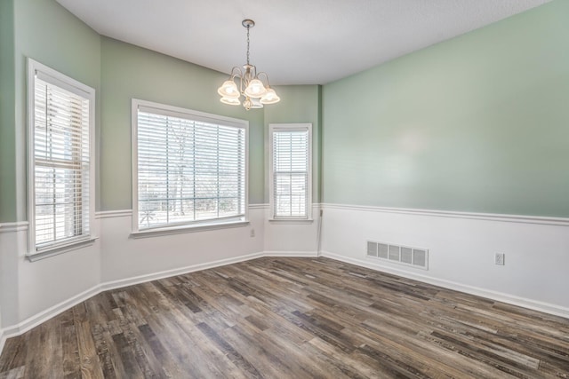 empty room with dark wood-type flooring and a notable chandelier