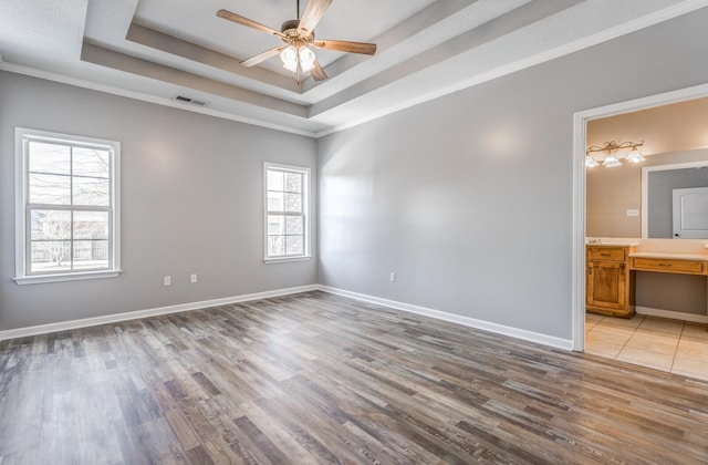 spare room featuring a raised ceiling, light wood-type flooring, a wealth of natural light, and crown molding