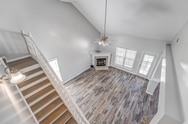 unfurnished living room with ceiling fan, high vaulted ceiling, a tile fireplace, and hardwood / wood-style floors