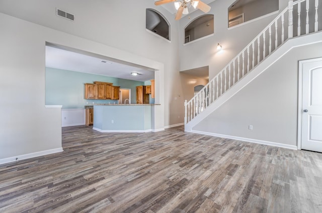 unfurnished living room featuring a high ceiling, ceiling fan, and wood-type flooring