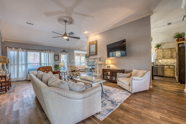 living room featuring ceiling fan, dark hardwood / wood-style flooring, crown molding, and a stone fireplace