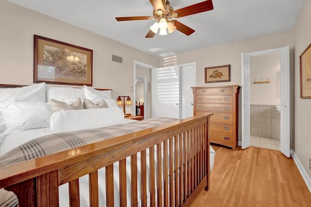 bedroom featuring ceiling fan, connected bathroom, light hardwood / wood-style flooring, and tile walls