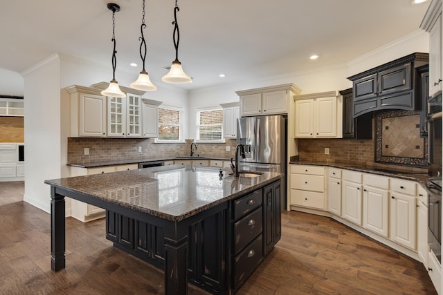 kitchen featuring stainless steel refrigerator with ice dispenser, decorative light fixtures, dark stone countertops, a large island with sink, and sink