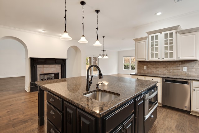 kitchen featuring dark stone countertops, a center island with sink, sink, a tiled fireplace, and appliances with stainless steel finishes