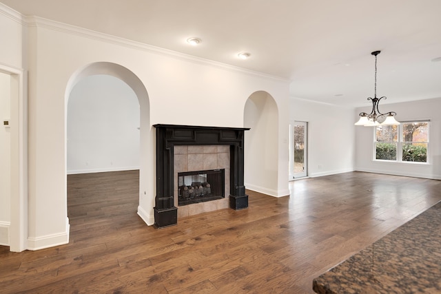 unfurnished living room featuring dark wood-type flooring, crown molding, a tile fireplace, and an inviting chandelier