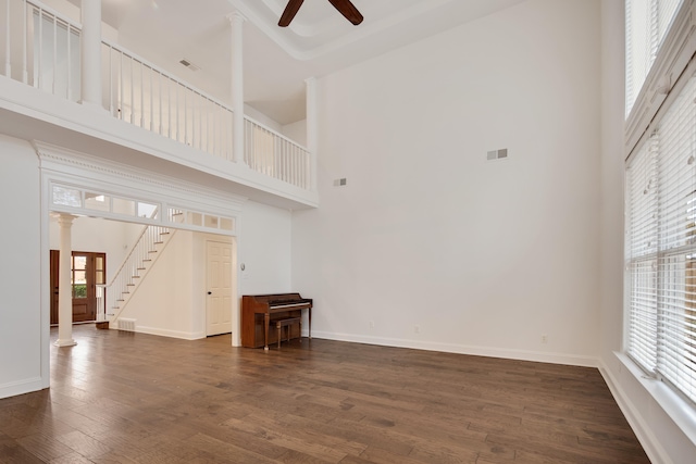 unfurnished living room with ceiling fan, a high ceiling, dark hardwood / wood-style flooring, and ornate columns