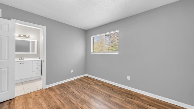 unfurnished bedroom featuring ensuite bath, sink, a textured ceiling, and light hardwood / wood-style flooring