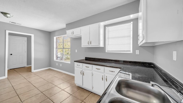 kitchen featuring a textured ceiling, light tile patterned floors, white cabinets, and sink