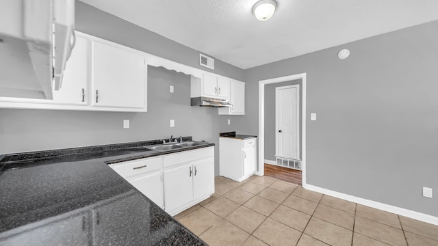 kitchen with light tile patterned floors, dark stone counters, a textured ceiling, white cabinets, and sink