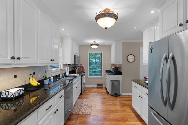 kitchen featuring appliances with stainless steel finishes, dark stone countertops, light hardwood / wood-style floors, and white cabinets