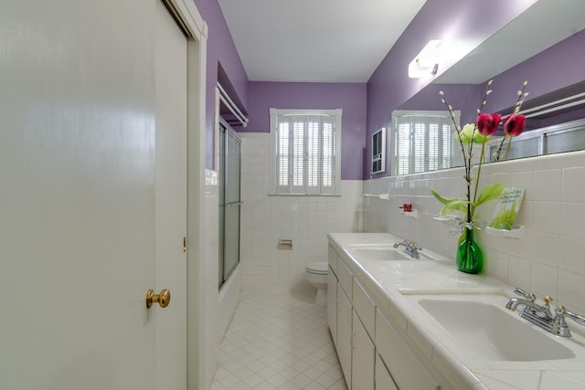 full bathroom featuring toilet, vanity, tile walls, tile patterned floors, and enclosed tub / shower combo