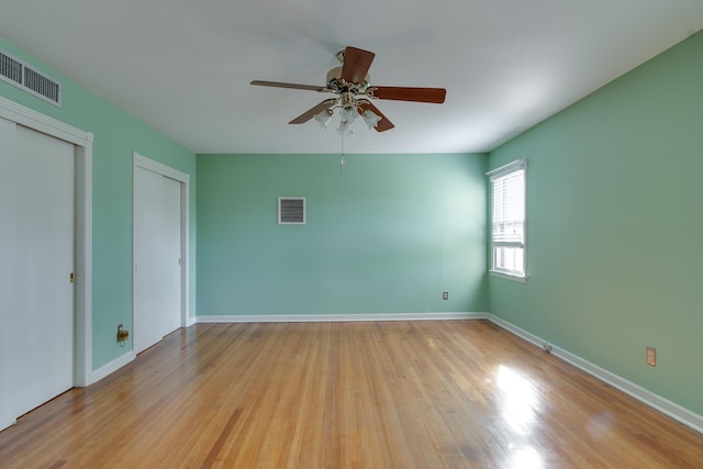 unfurnished bedroom with light wood-type flooring, ceiling fan, and multiple closets