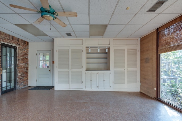 unfurnished living room with ceiling fan, a paneled ceiling, brick wall, and wooden walls