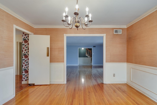 empty room with hardwood / wood-style flooring, ornamental molding, and a chandelier