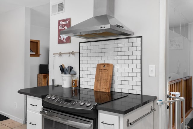 kitchen featuring backsplash, range hood, stainless steel electric range, light tile patterned flooring, and white cabinets